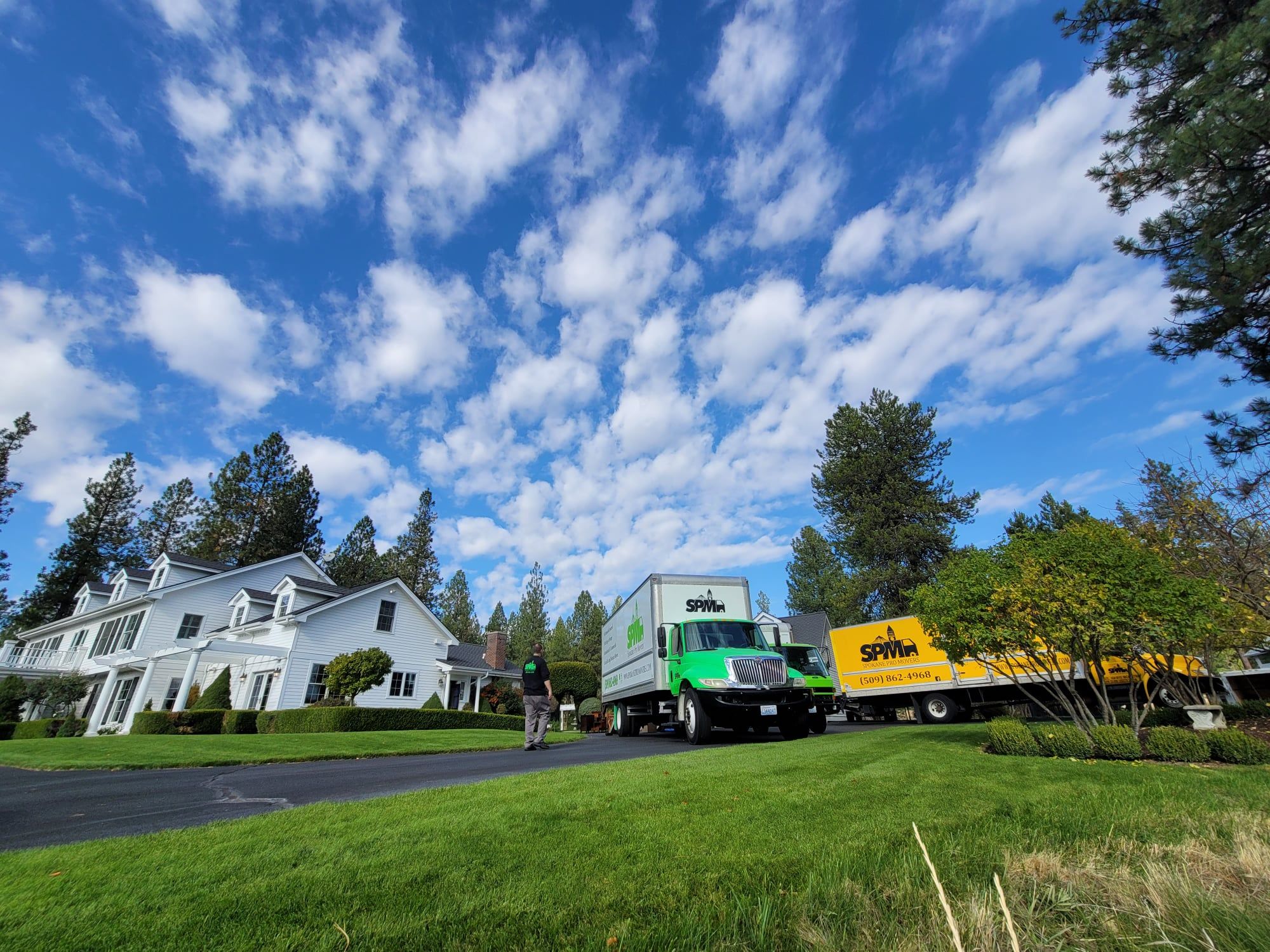 Two branded Spokane Pro Movers trucks parked at a Spokane-area home on a clear day